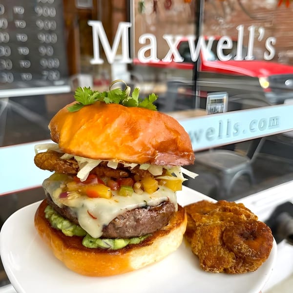 A Maxwell's burger with guacamole, melted cheese, salsa, and fried plantains on a white plate.