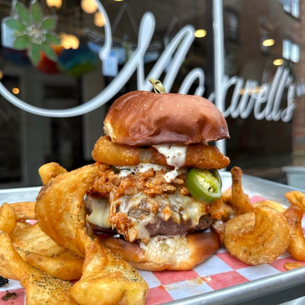 A Maxwell's burger with chili, cheese, onion rings, and jalapeños, served with curly fries.