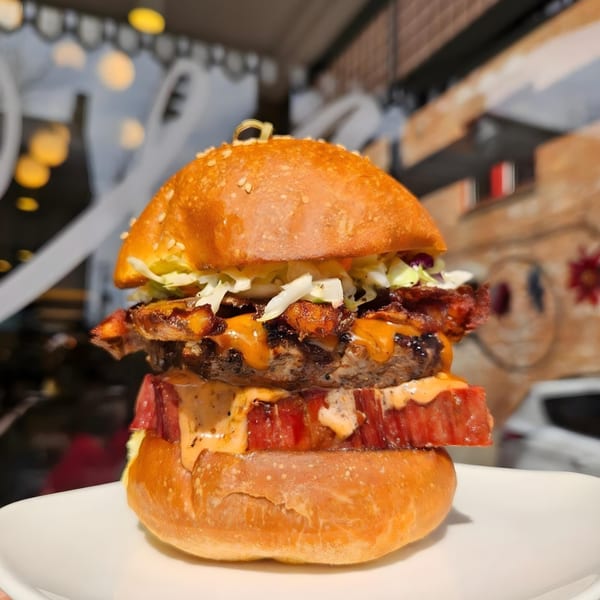 A Maxwell's burger with a thick patty, bacon, cheese, lettuce, and sauce on a sesame bun.