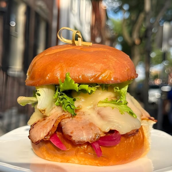 A Maxwell's burger with bacon, melted cheese, lettuce, and pickled onions on a brioche bun.